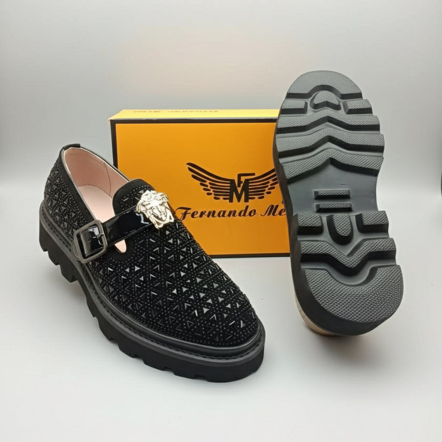 Black shoe with decorative buckle and crystal, displayed with a brand box in the background.