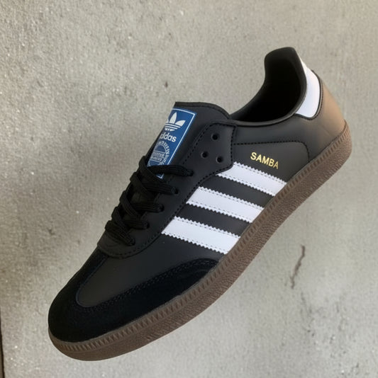 Black Adidas Samba sneaker with white stripes held by a hand on a neutral background