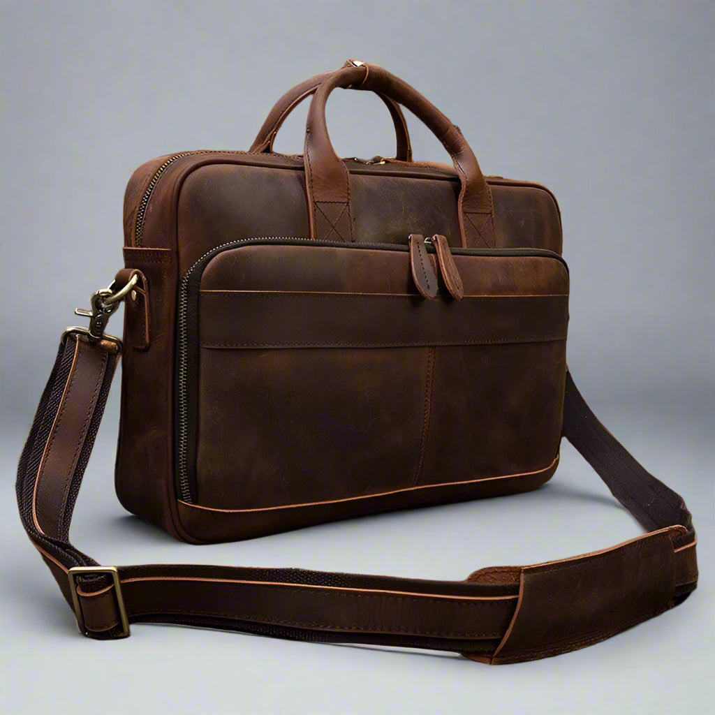 Brown leather briefcase with shoulder strap on a wooden surface