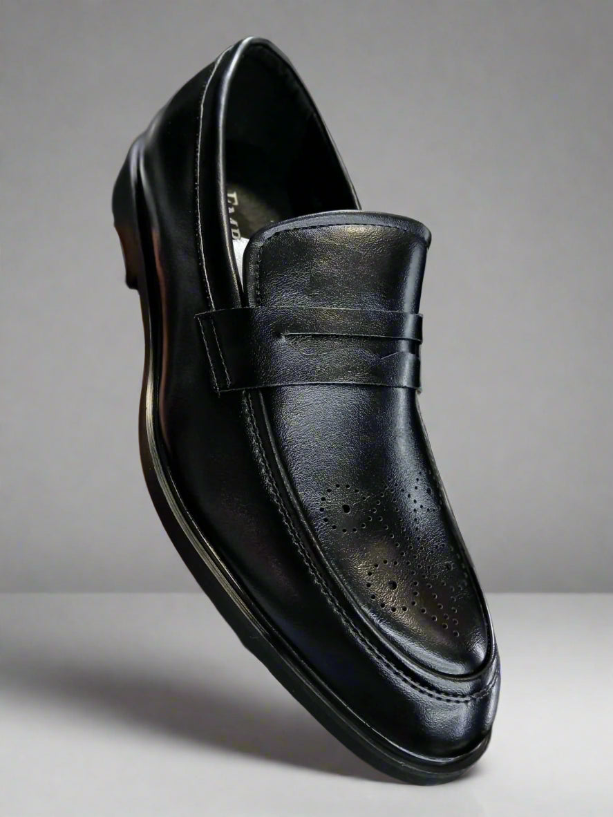 Black leather loafer shoe held by a hand with a blurred background