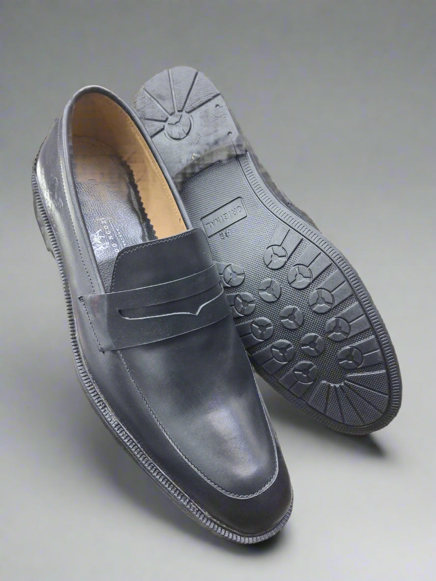 Dark gray loafers with black soles held by a person indoors.