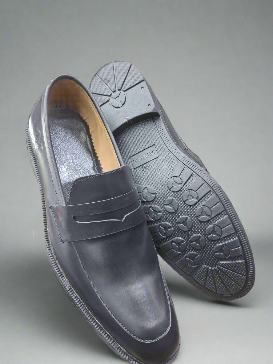 Black loafer shoe with a textured sole held by a person.