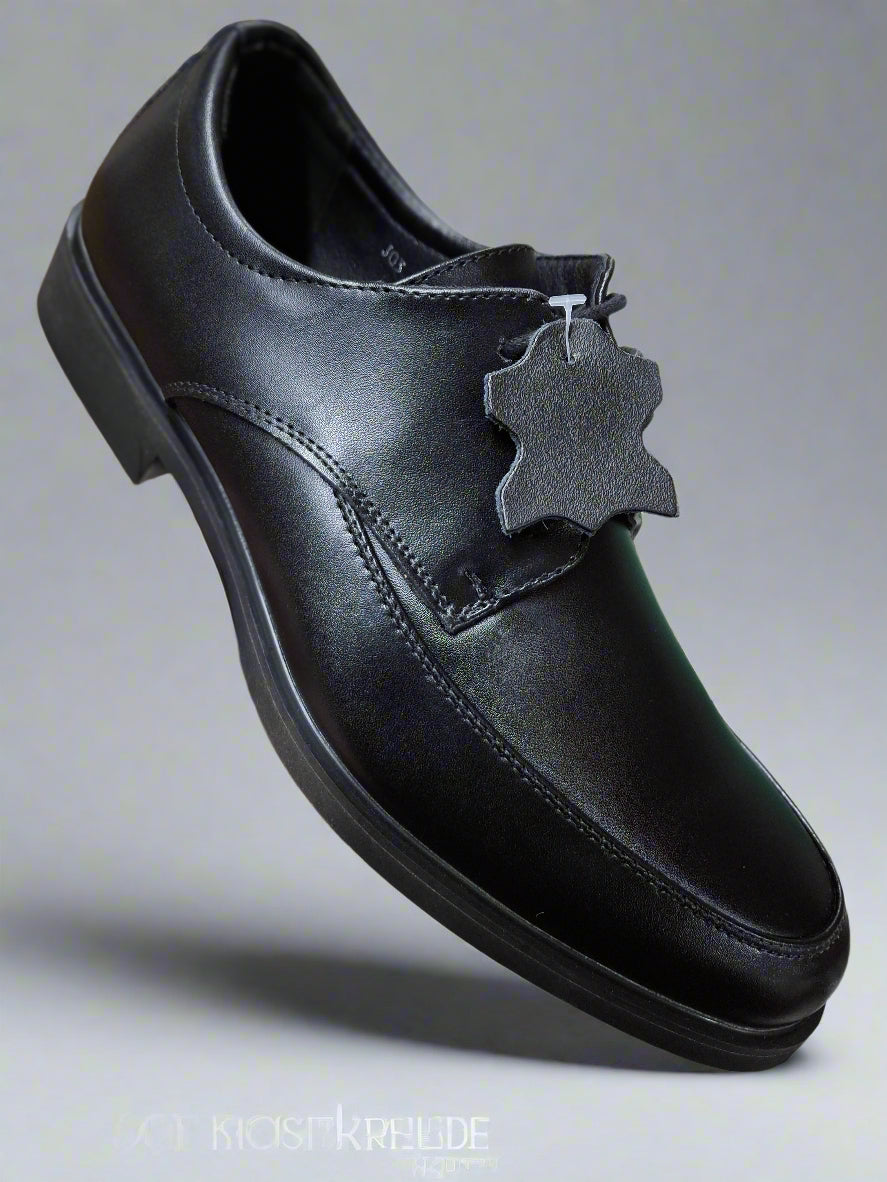 Black leather shoe held by a hand on a tiled floor
