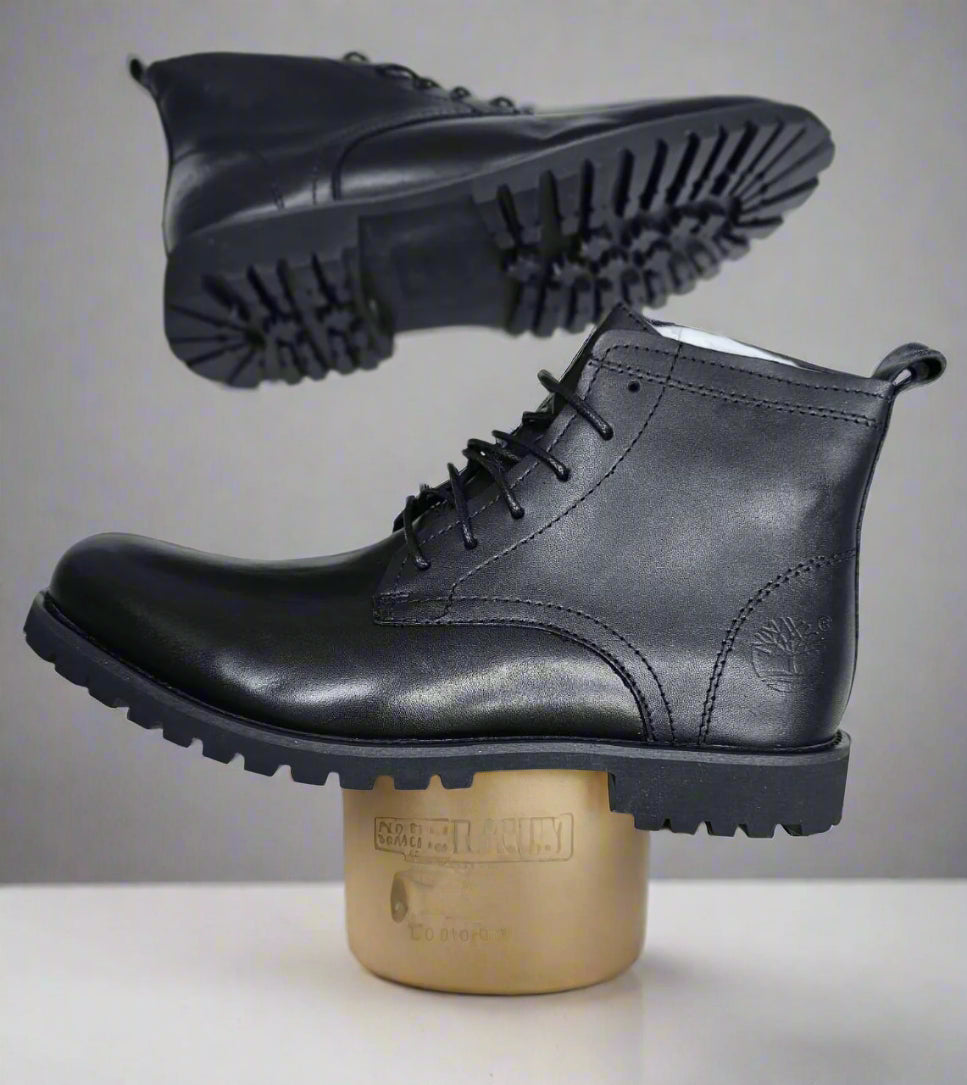 Black leather boots held by a hand on a light gray tiled floor