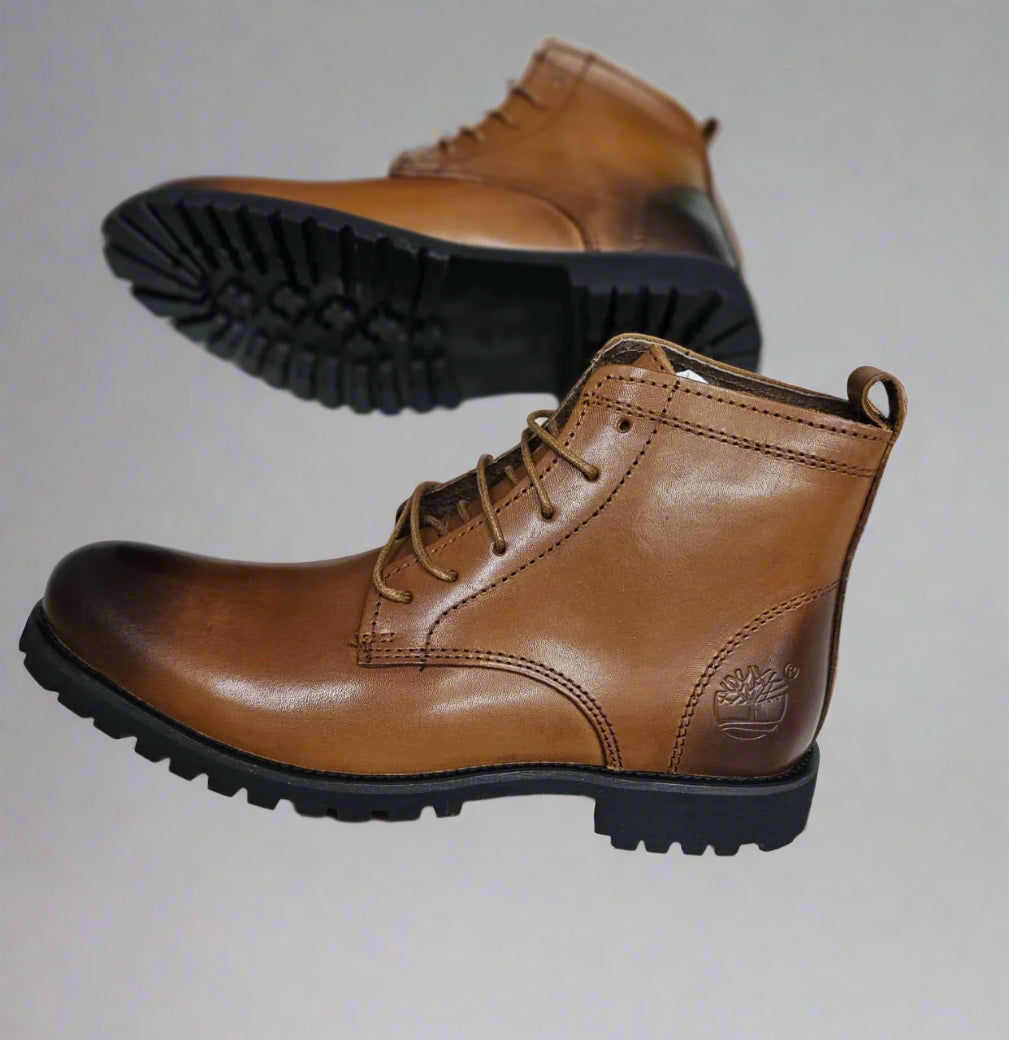Brown leather boot held by a hand on a light gray floor.