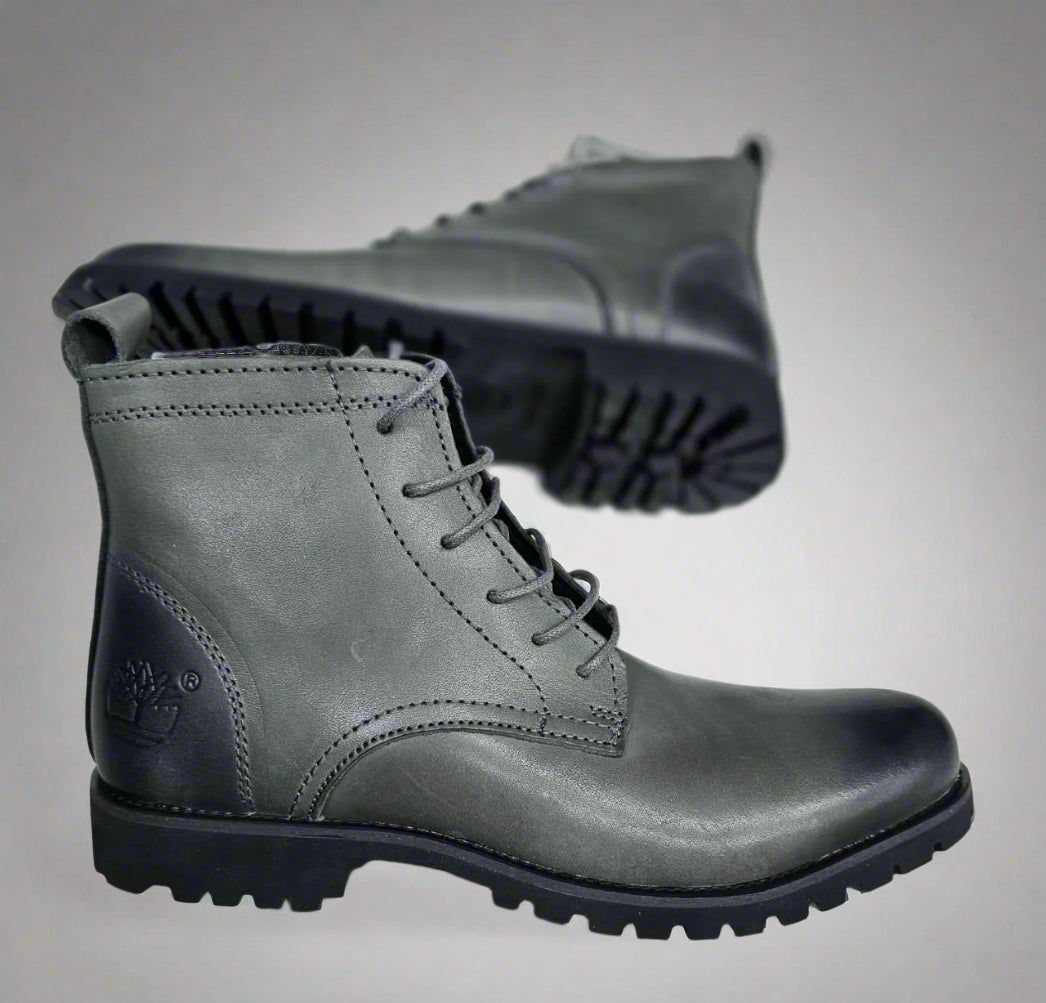 Gray leather boot held by a hand with a blurred background