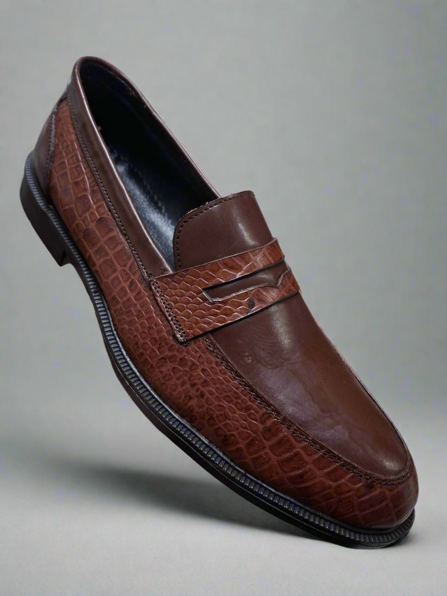 Brown leather loafer shoe held by a hand with a blurred indoor background