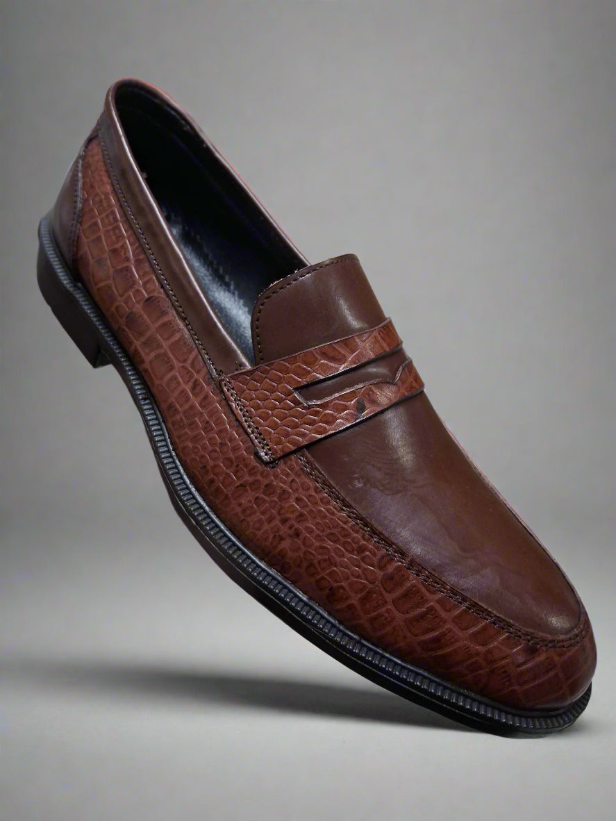 Brown leather loafer shoe held by a hand with a blurred indoor background