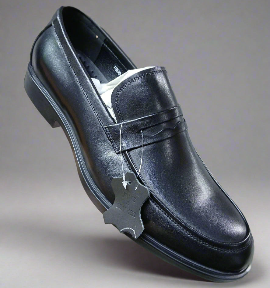 Black leather shoe held by a hand with a blurred indoor background