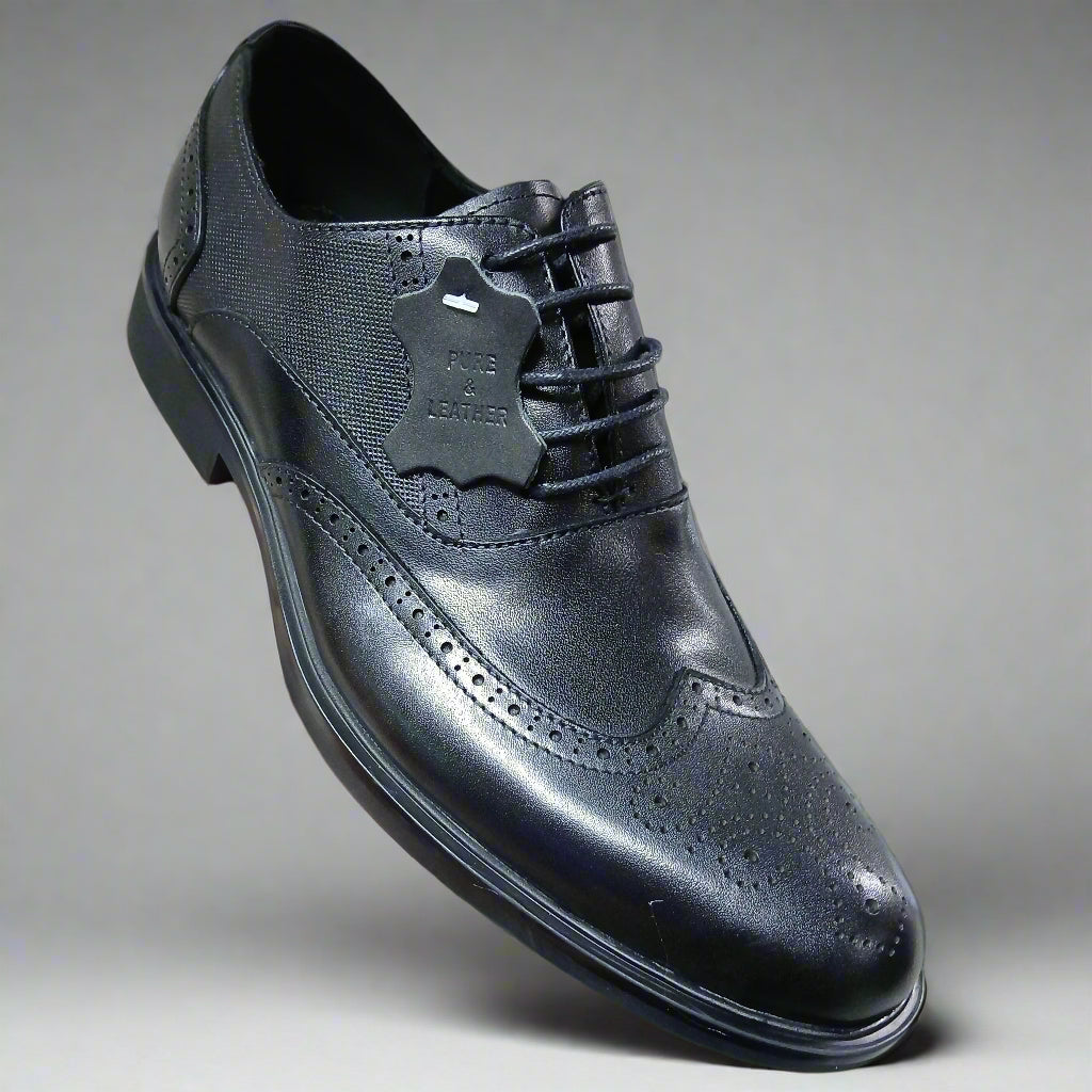 Black leather dress shoe held by a hand with a blurred indoor background