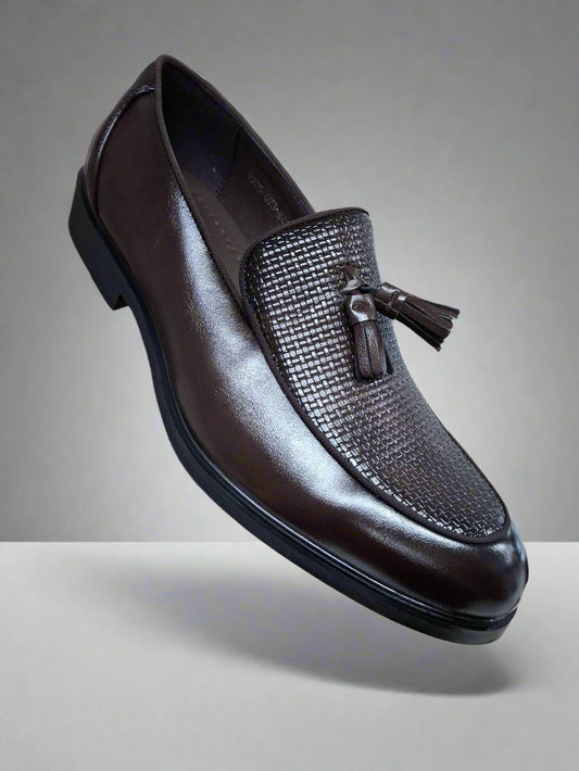 Brown leather loafer with tassel held by a hand against a blurred indoor background