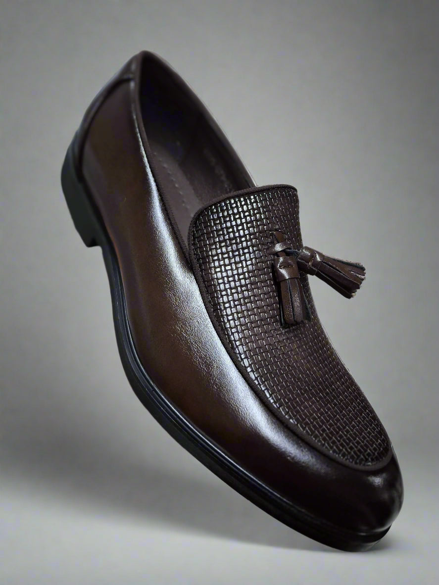 Brown leather loafer with tassel held by a hand on a tiled floor.