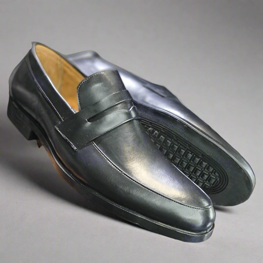 Black leather loafer held by a person with a blurred background
