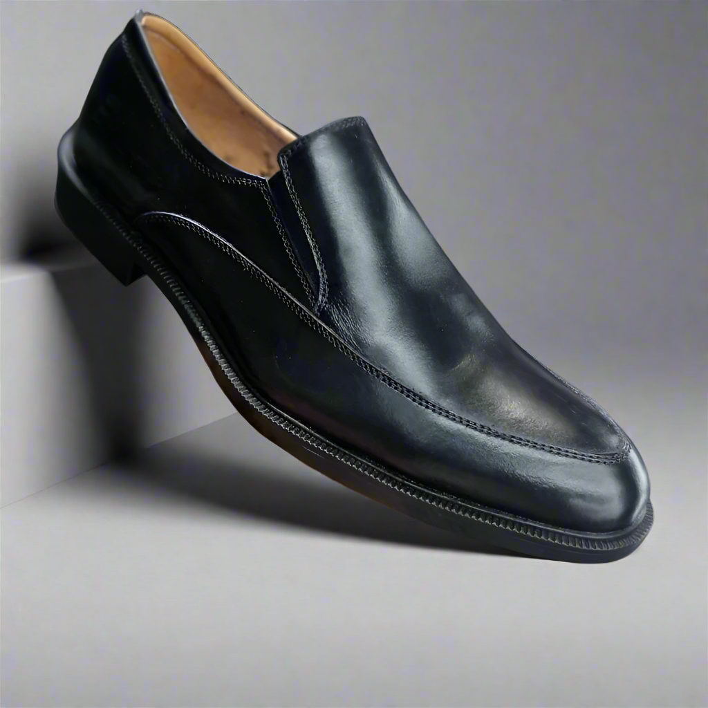 Black leather loafer shoe held by a hand on a white background