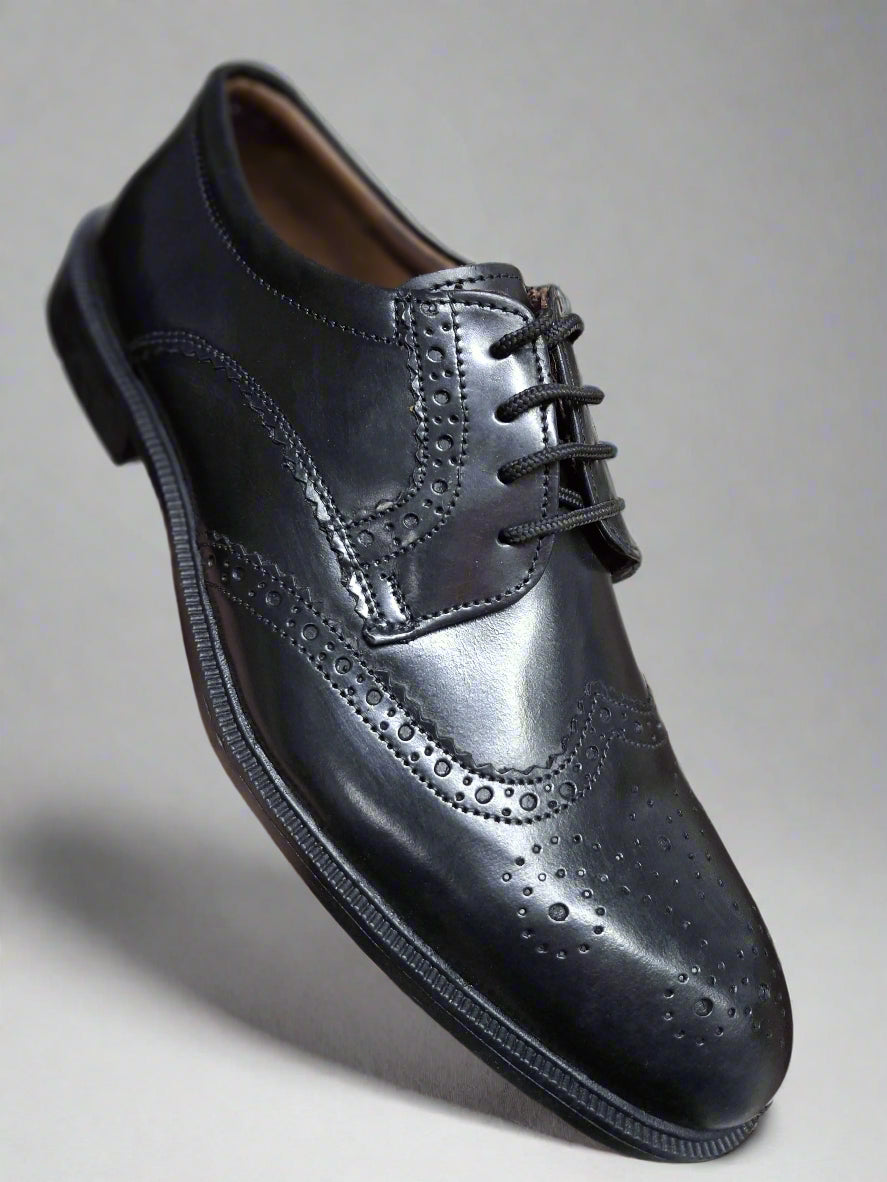 Black leather dress shoe held in a hand with a blurred background