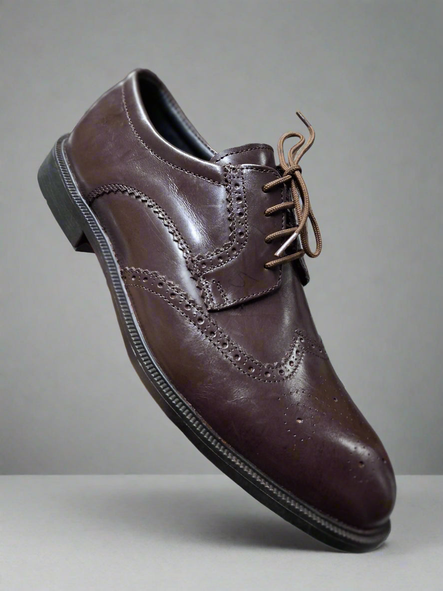 Brown leather dress shoe held by a hand with a blurred indoor background