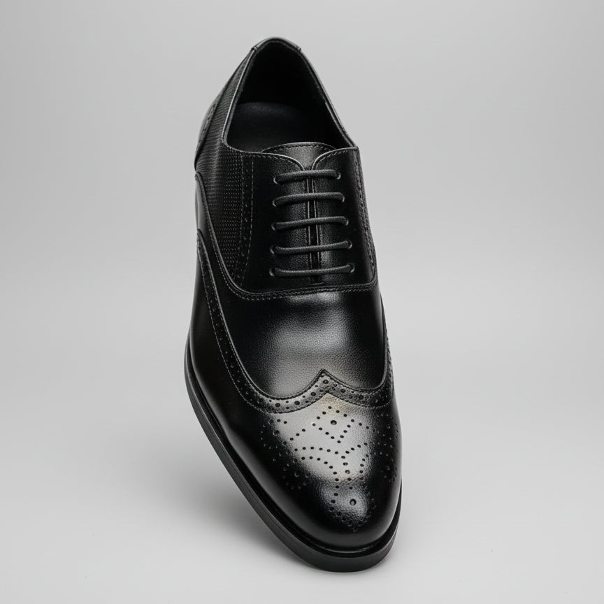 Black leather dress shoe held by a hand with blurred shelves in the background