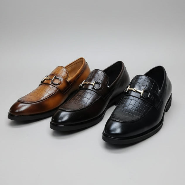 Three men's loafers in brown, black, and blue on a cardboard box with visible branding.