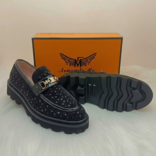 Black loafers with gold buckle and orange box in the background, featuring the brand logo.