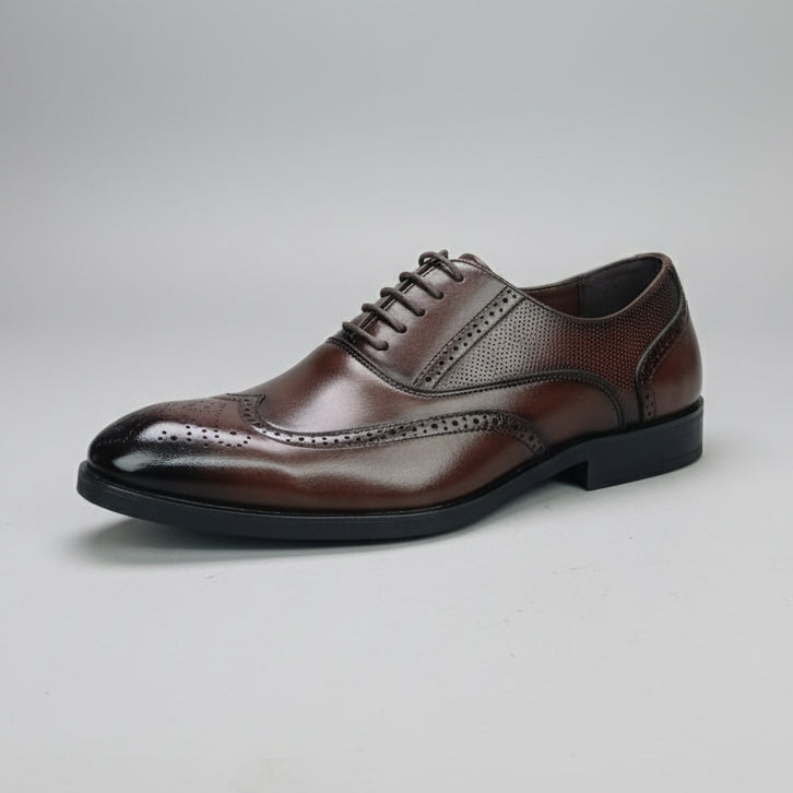 Hand holding a brown leather dress shoe with a blurred background of shoes on shelves.