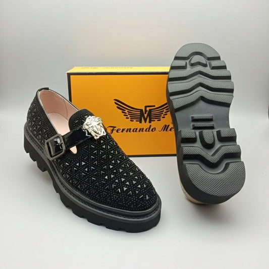 Black shoe with decorative buckle and crystal, displayed with a brand box in the background.