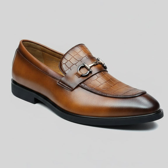 Brown leather shoe with a decorative buckle held by a hand against a blurred background