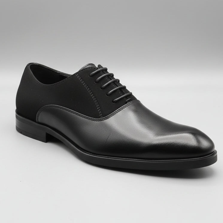 Black dress shoe held by a hand with a blurred background