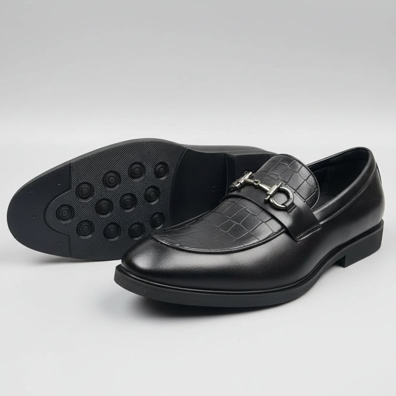 Black dress shoes with a textured sole on a concrete surface with cardboard boxes in the background.