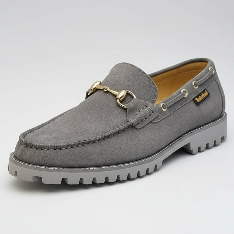 Gray suede loafer held by a hand with a blurred background