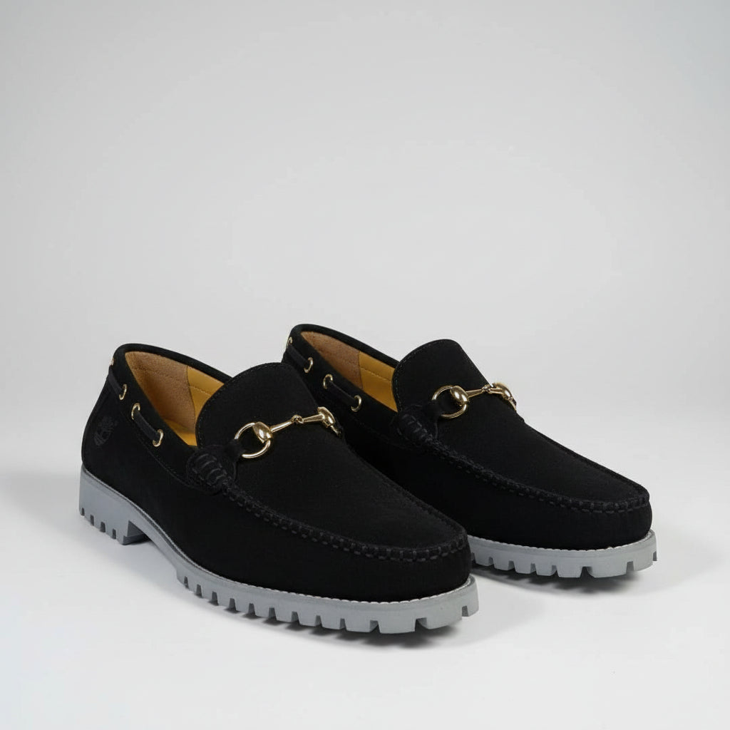 Pair of black loafers with gold buckles on a textured surface