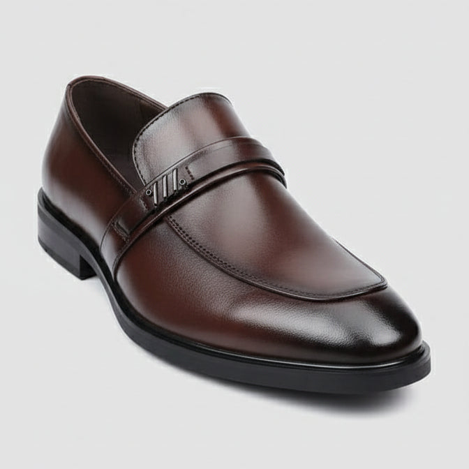 Brown leather shoe held by a hand with a visible brand tag, blurred background of shoes and stones.