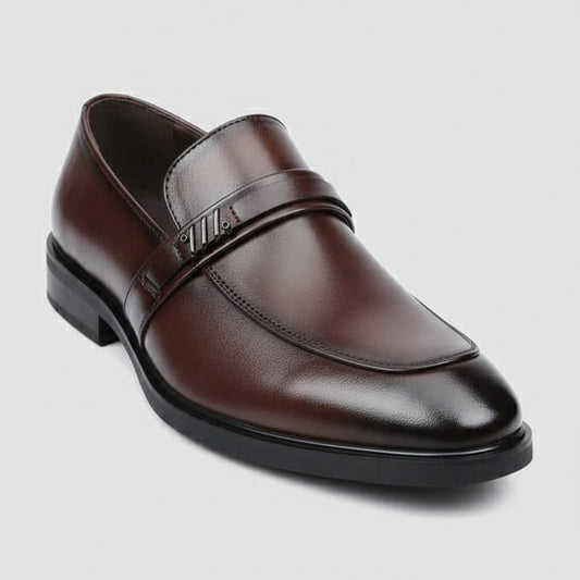 Brown leather shoe held by a hand with a visible brand tag, blurred background of shoes and stones.