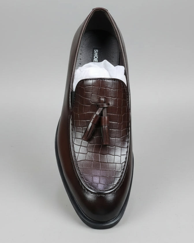 Brown leather shoe with tassel held by a person against a cluttered background