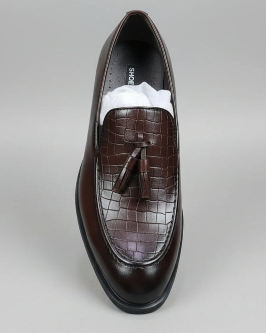 Brown leather shoe with tassel held by a person against a cluttered background