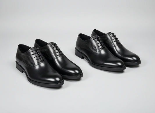 Four black dress shoes on a textured surface