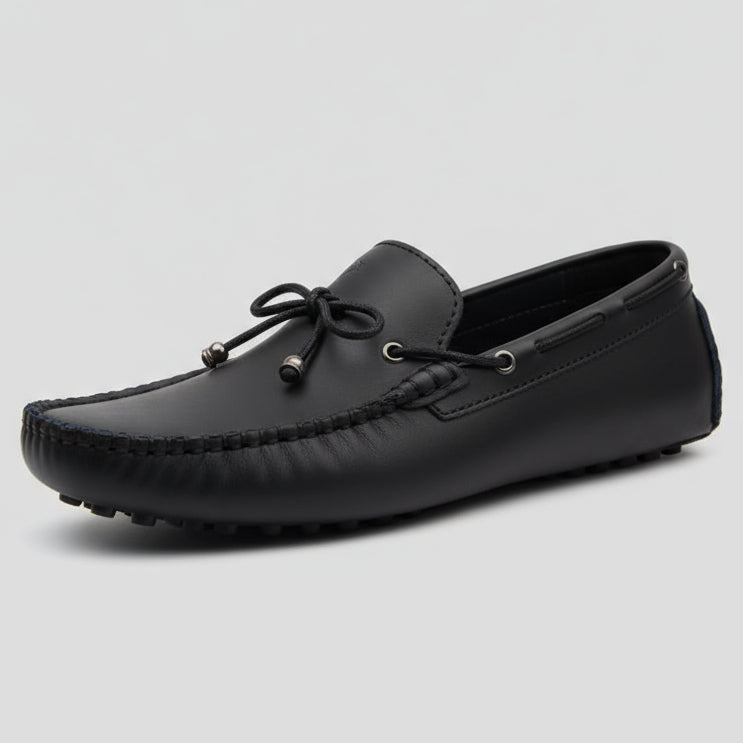 Black loafer shoe held by a hand with a blurred background
