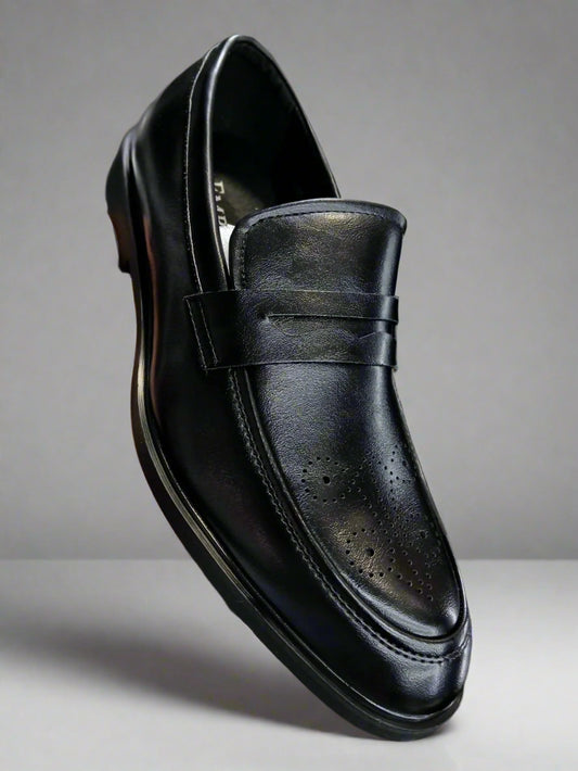 Black leather loafer shoe held by a hand with a blurred background