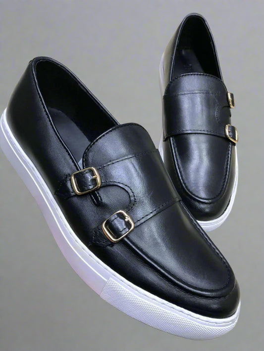 Black leather shoes with gold buckles held by a hand on a light background
