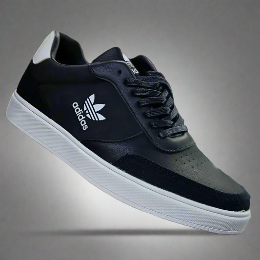 Black Adidas sneaker held in a hand with a blurred shoe store background