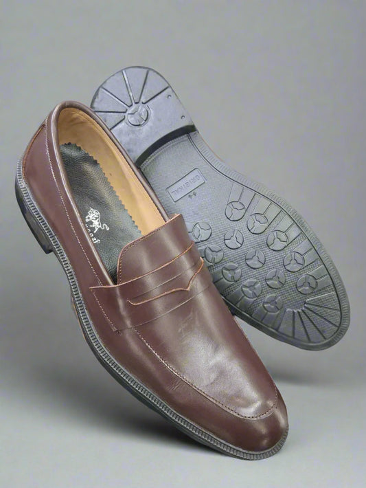 Brown leather loafer shoe with gray sole held by a person, blurred background of shoes.