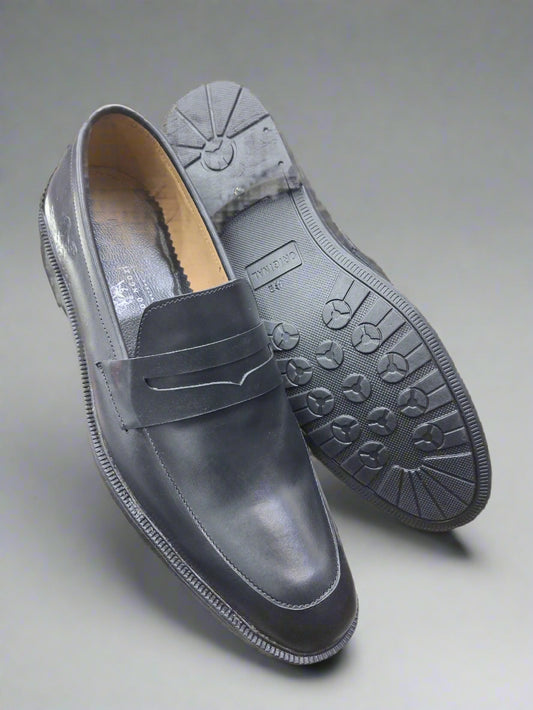 Dark gray loafers with black soles held by a person indoors.