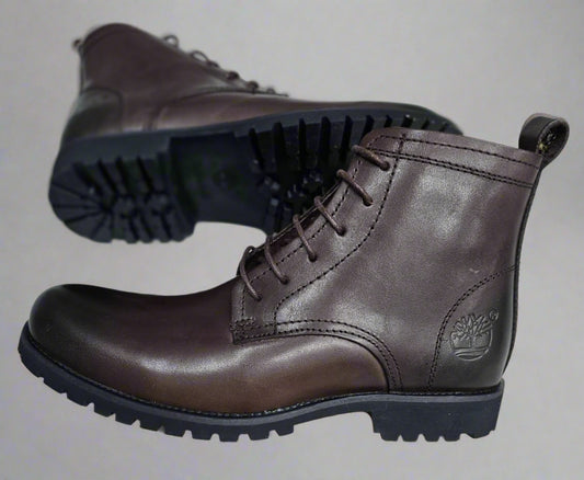 Brown leather boots with black soles held by a hand on a light background