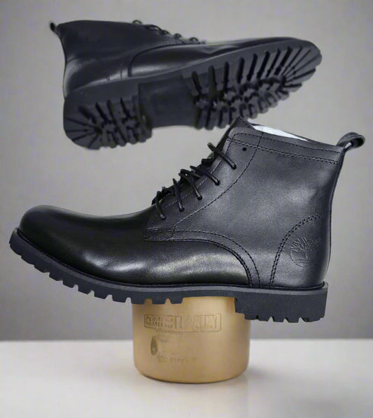 Black leather boots held by a hand on a light gray tiled floor