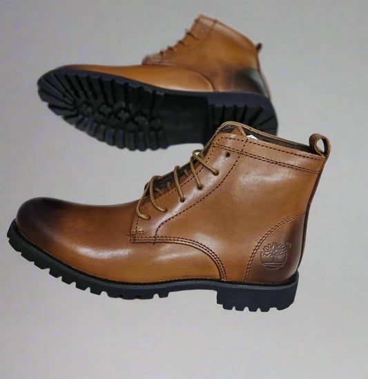 Brown leather boot held by a hand on a light gray floor.