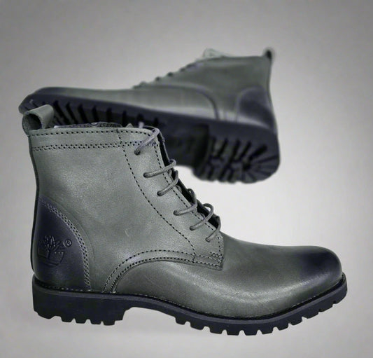 Gray leather boot held by a hand with a blurred background
