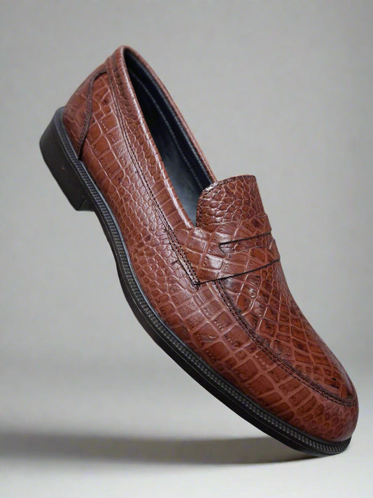 Brown textured loafer shoe held by a person against a blurred background