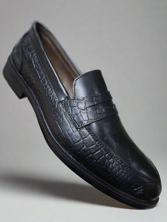 Black leather shoe held by a hand on a tiled floor background