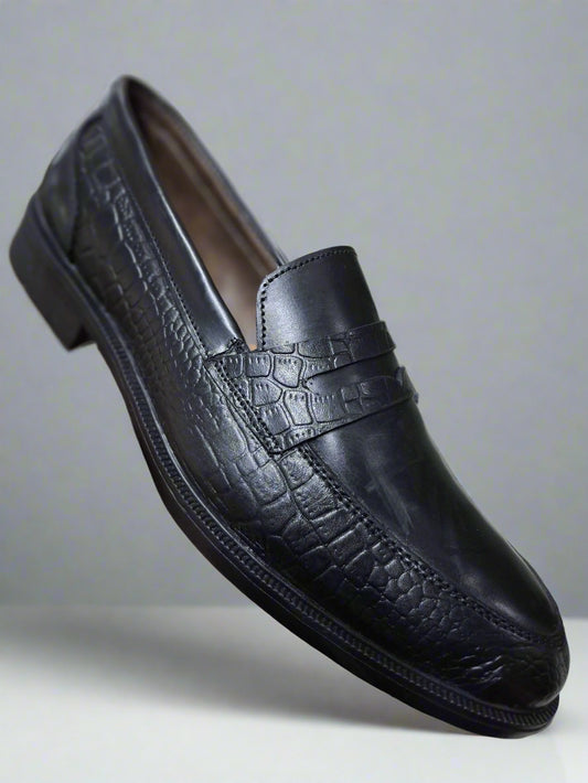 Black leather shoe held by a hand on a tiled floor background