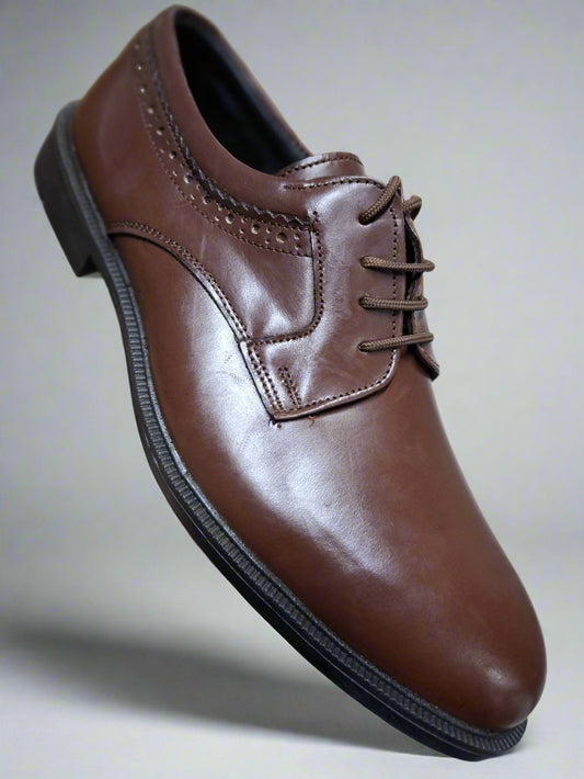 Brown leather dress shoe held by a hand on a tiled floor.