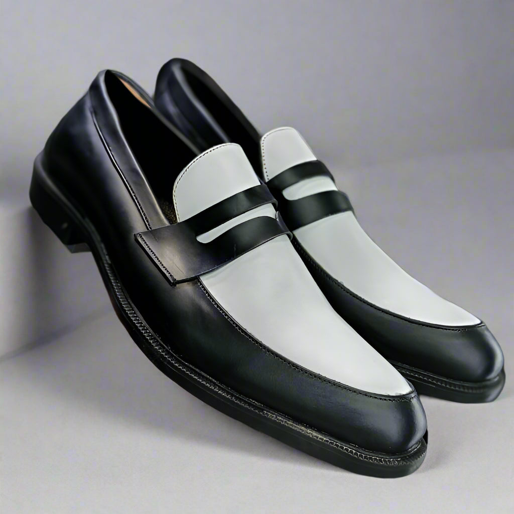 Black and white loafers held by a person with a blurred background of shoes.